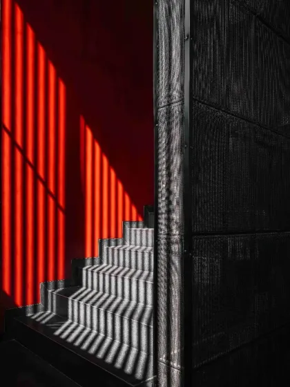 The dramatic play of light and shadow across a staircase in Project 1374. A bright red wall is activated by linear shadows, transforming a simple circulation space into a dynamic visual composition.