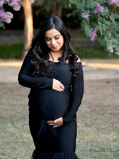 A moment of connection in nature. The mom-to-be gently holds her bump, surrounded by greenery and soft purple flowers in this lovely outdoor shot.