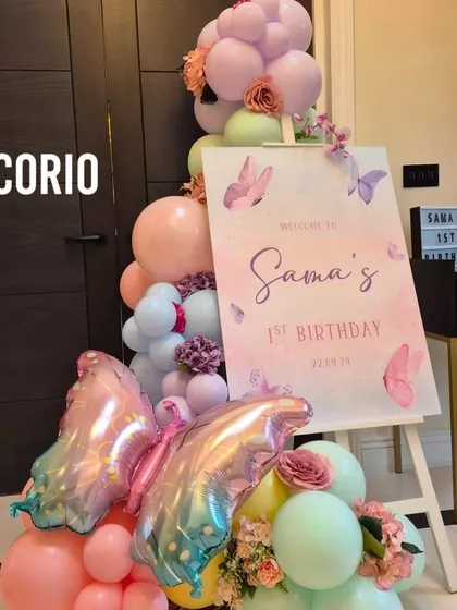 A beautiful welcome sign for 'Sama's 1st Birthday', decorated with a pastel balloon arrangement and iridescent butterfly foil balloons.