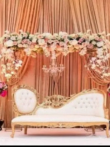 I design elegant reception stages perfect for classic weddings. This setup features a beautiful floral arch, a vintage-style diwan sofa, and soft golden lighting for a timeless and romantic feel.