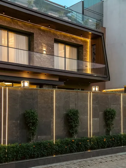 The boundary wall of Club Drive House features integrated linear lighting, which highlights the texture of the stone panels and creates a dramatic effect at night.