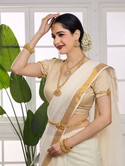 A graceful pose highlighting a complete temple jewellery set, including necklaces, earrings, and a waist belt. The model is styled in a classic South Indian saree, creating an authentic and aspirational look for ethnic jewellery brands.