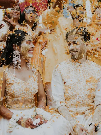 A beautiful candid shot of Nikita and Akash during their Haldi, completely covered in turmeric and flower petals, sharing a joyful laugh. These are the memories that last a lifetime.