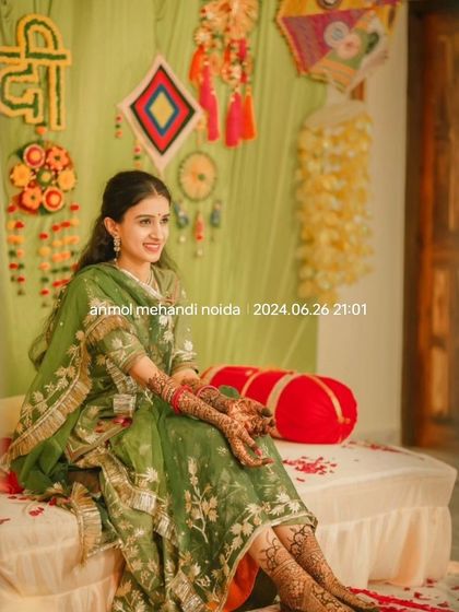 A full-length shot of the bride seated at her mehendi ceremony, showcasing her complete look from her outfit to her hand and foot mehendi.