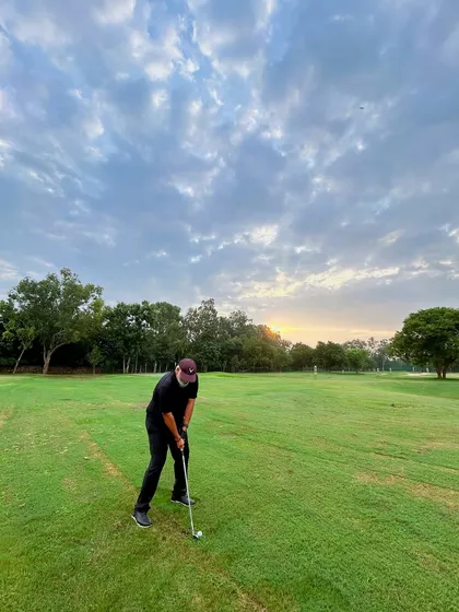 A lone golfer practices his swing on the grass as the sun sets in the background.
