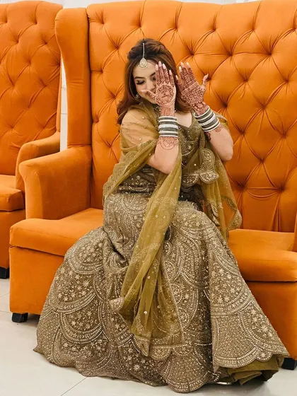 A shy bride showing off her beautiful henna. She is wearing a gorgeous olive-gold lehenga with intricate all-over embroidery, a perfect rental choice for a mehendi or the wedding day itself.