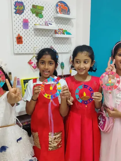 A group of friends posing with their finished Diwali crafts. Their smiles and festive outfits add to the cheerful atmosphere.