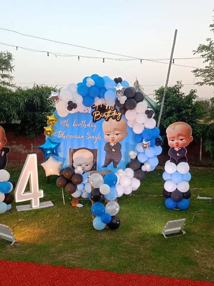 An outdoor Boss Baby theme for a 4th birthday. This setup includes a custom backdrop, character cutouts, and a blue, black, and white balloon arch, perfect for a garden or lawn party.