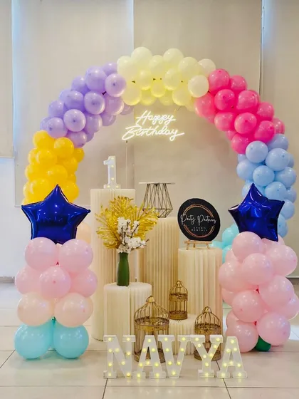 Sometimes, simple and sweet is the way to go. This minimalist setup for Navya's first birthday features a lovely pastel rainbow balloon arch, a neon sign, and elegant plinths for a clean and modern look.