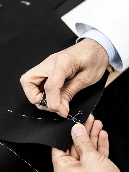 True craftsmanship is in the hands of the artisan. Here, a tailor works on the fine hand-stitching of a lapel, a detail that ensures the garment holds its shape and elegance for years to come.