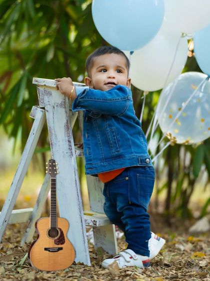A classic toddler portrait taken outdoors. The combination of a cute outfit, simple props like balloons and a guitar, and natural light creates a beautiful memory.