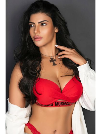 A portrait featuring a bold red bra top and an open white shirt. The focus is on the model's strong expression and the vibrant color contrast of the styling.