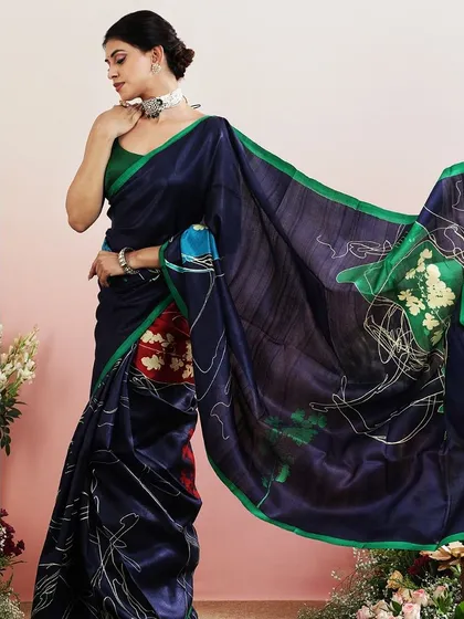 The flowing pallu of the navy and green saree creates a beautiful, artistic effect.