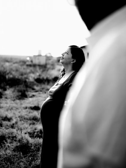 A beautifully composed black and white shot, taken from over the partner's shoulder. The mom-to-be looks up with a hopeful expression, creating an intimate and artistic portrait.