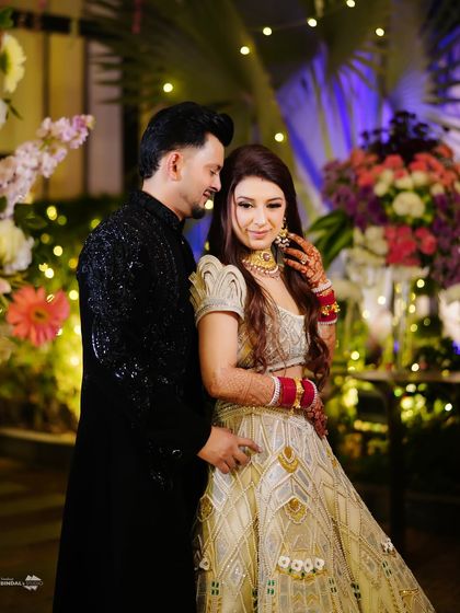 A classic reception portrait. The couple poses against a backdrop of beautiful floral arrangements and fairy lights, looking elegant and happy.