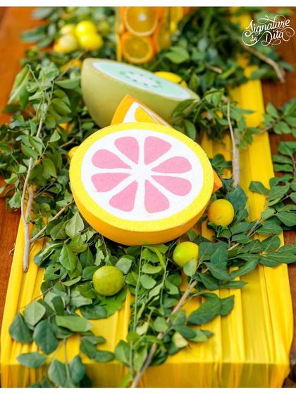 A table runner made from yellow fabric, lush greenery, and hand-painted citrus props. This creates a rich and textured look for the dining tables.