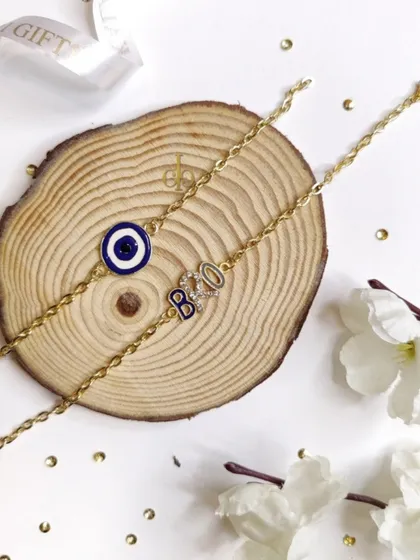 A close-up of our "Bro" initial and evil eye Rakhi bracelets, featuring a stylish gold chain.
