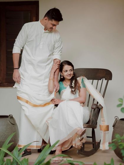 A classic portrait of the couple, the groom standing by his seated bride in a rocking chair.