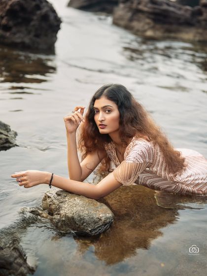A close-up shot of the model in a sequined gown, lying in the water. The way the light hits the wet fabric and the water creates a beautiful, shimmering effect.