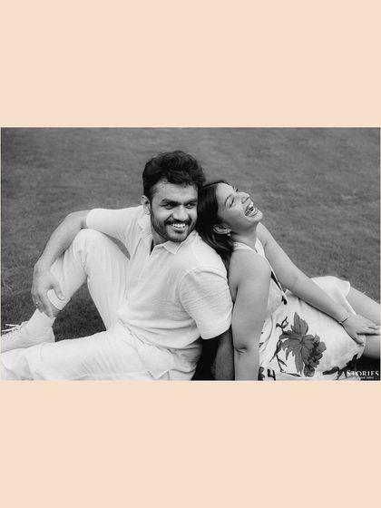 A joyful black and white portrait of the couple sitting back-to-back on the grass, sharing a laugh.