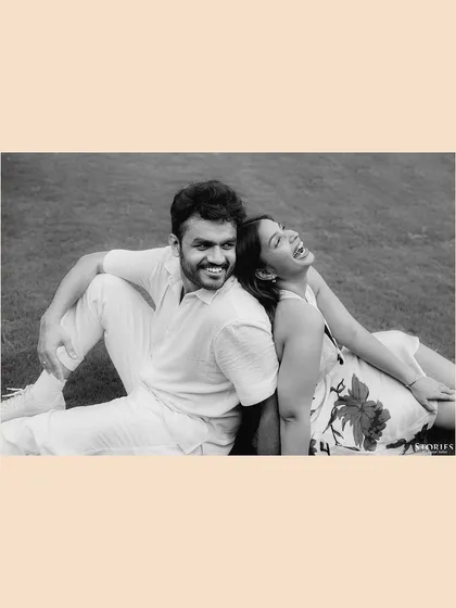 A joyful black and white portrait of the couple sitting back-to-back on the grass, sharing a laugh.