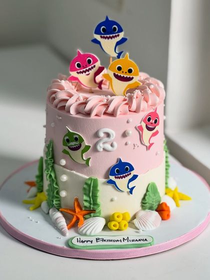 Baby Shark, doo-doo-doo! This cute and colorful cake is perfect for a 2nd birthday, featuring the whole shark family, edible seaweed, and seashell details for an ocean of fun.