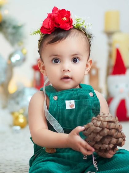 A close-up of a baby girl holding a pinecone in our Christmas setup. We focus on capturing their curiosity and wonder during the holidays.