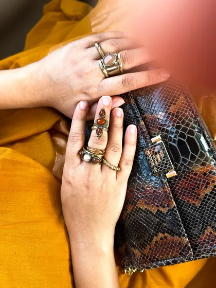 A detail shot of my hands, showing the stacked rings and the texture of the snakeskin clutch against the yellow khadi saree.