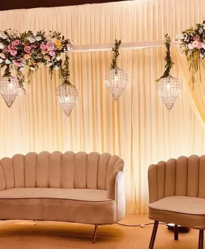 A classic reception stage with soft yellow drapery and hanging crystal birdcage lanterns. The pink and white floral arrangements add a touch of romance to this warm and inviting setup.