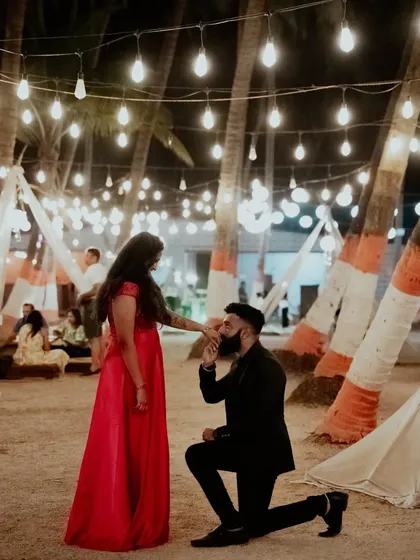 A grand gesture of love, with the groom-to-be kissing his partner's hand under a canopy of lights at a beachside location.