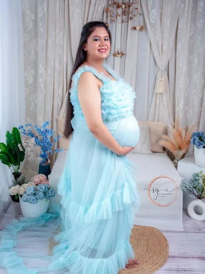 Feeling like a queen in one of our beautiful studio gowns. This solo portrait showcases a lovely mom-to-be in a light blue ruffled dress, highlighting the elegance and grace of motherhood.