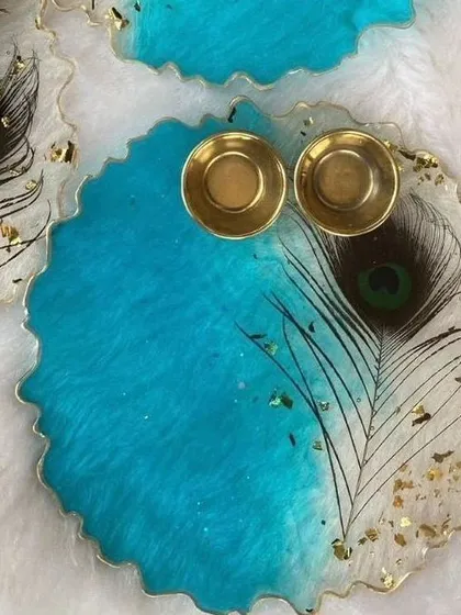 A unique Rakhi platter design featuring a real peacock feather preserved in resin. The vibrant blue and clear sections are complemented by gold flakes, creating an elegant and symbolic piece.