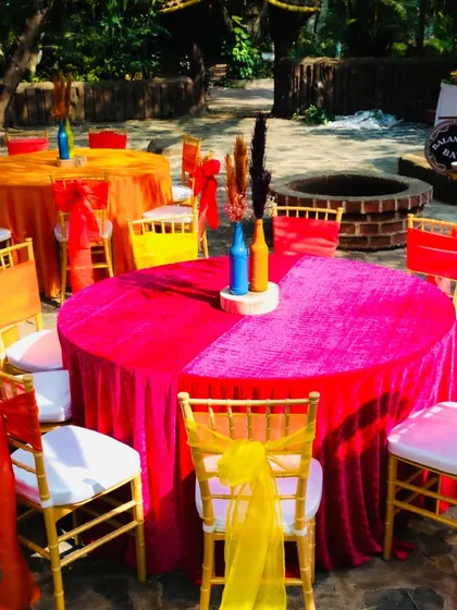 Bright and bold table setups, using velvet tablecloths in shades of magenta and orange, complemented by colorful chair sashes.