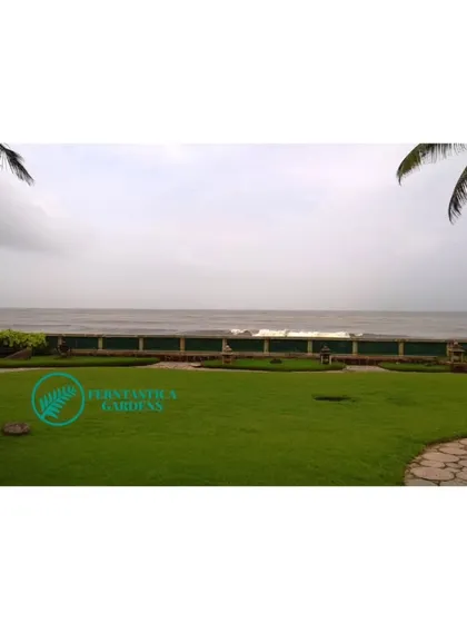 A pristine lawn at a seafront villa, framed by two coconut palms. The open green space provides an unobstructed, breathtaking view of the sea.