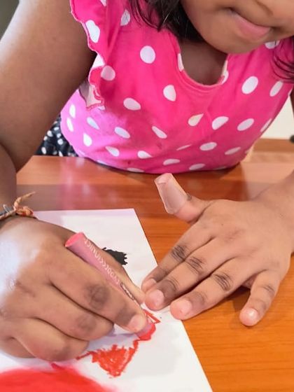 A close-up shot of small hands carefully applying color with an oil pastel. We help even our youngest students develop fine motor skills through art.