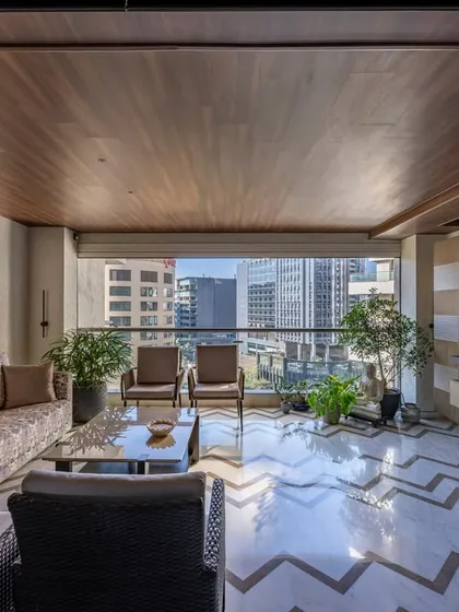 This living area opens onto a balcony with stunning city views. We used a chevron-patterned marble floor and a wooden ceiling to add texture and warmth, blurring the lines between indoor and outdoor living.