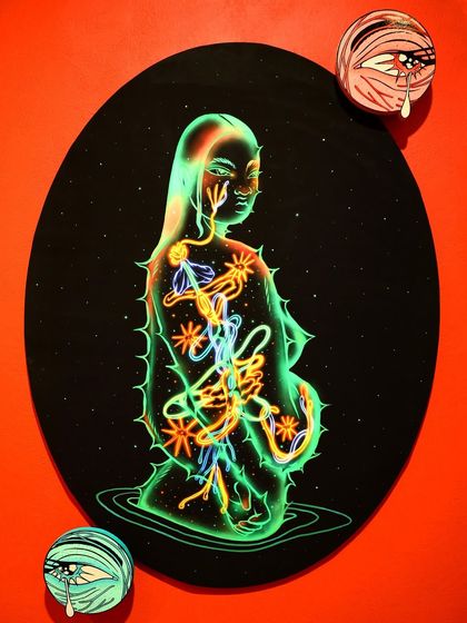 My artwork 'Bioluminescence I' exhibited as a physical print, mounted on an oval board against a vibrant red wall, showing how my digital work translates to a gallery setting.