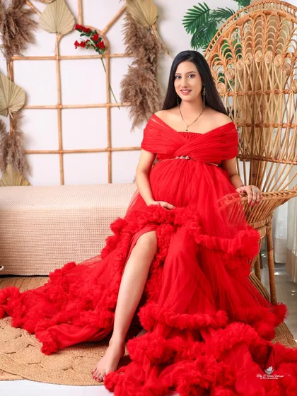 A confident and glamorous solo shot. The mom-to-be is seated on a large peacock chair, the bold red of her gown making a powerful and stylish statement.