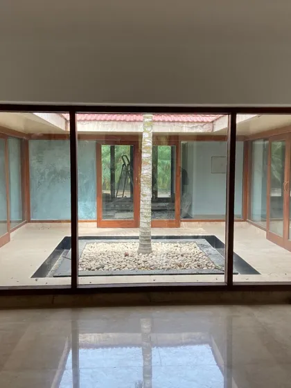 At the heart of our design philosophy is the integration of nature. This farmhouse is designed around a central courtyard, blurring the lines between indoors and outdoors. The glass walls flood the interiors with natural light and offer constant views of the serene central tree, embodying our approach to biophilic design.