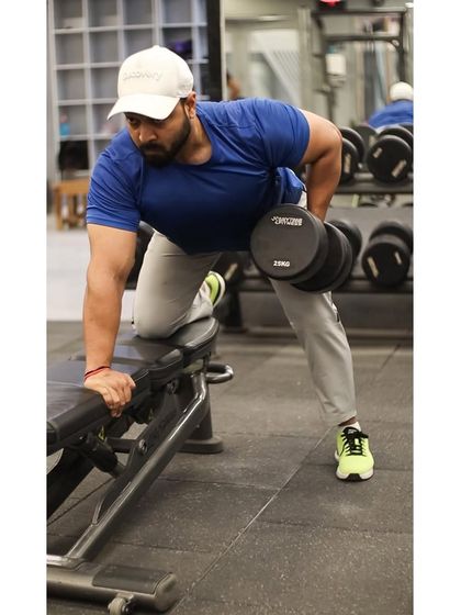 A member performs a single-arm dumbbell row on a bench, a unilateral exercise that helps build a strong back and correct muscle imbalances.