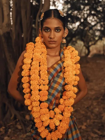 A powerful, direct portrait where the marigold garland frames the model's face. Her strong gaze and the rustic setting create a captivating image of raw, natural beauty.