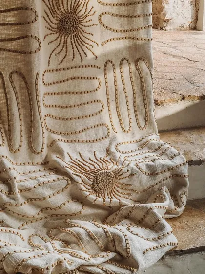 Craftsmanship is at the heart of our collections. This close-up reveals the artistry of our 'Perpétuel Soleil' fabric, where each wooden bead is meticulously hand-embroidered onto a linen base to create a design that is both tactile and visually captivating.
