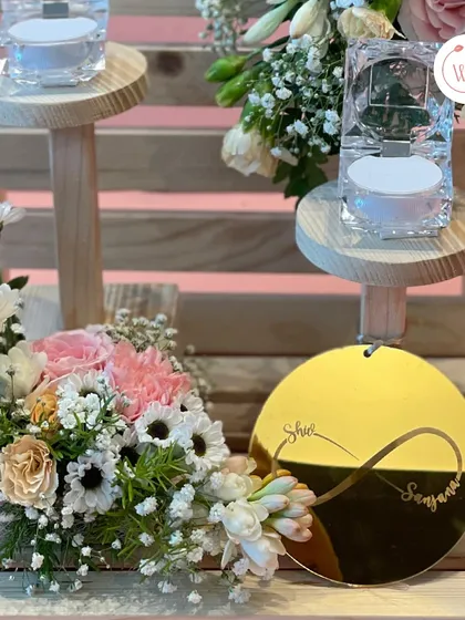 A close-up of a personalized ring platter. This design features a rustic two-tiered wooden stand, crystal ring holders, and a custom gold acrylic tag with the couple's names entwined in an infinity symbol.