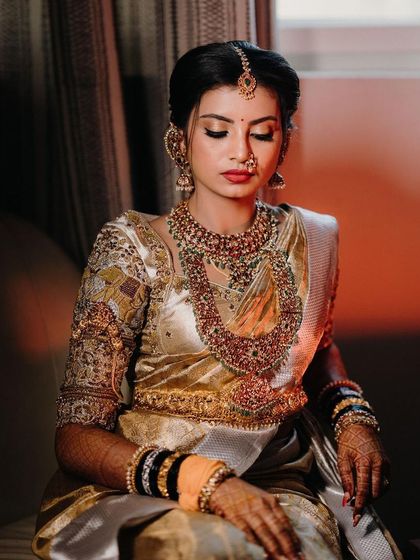 A dramatic portrait of the bride, her face illuminated in the dark. The focus is on her traditional jewelry and the rich texture of her saree.