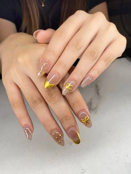 A cute and elegant design. These almond nails have a nude base with gold chrome tips and are accented with 3D gold bows.