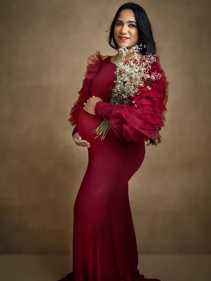 A full length portrait where the soft, glowing makeup complements the dramatic red dress perfectly. This is a classic maternity photoshoot look.