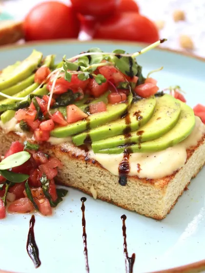 A close-up of our Open Avocado Toast, showing the beautiful layers of creamy hummus, sliced avocado, and fresh tomato salsa, all drizzled with balsamic glaze.