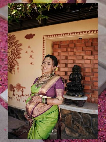 The mother-to-be stands beside traditional decor, her hand on her belly. This shot beautifully combines the personal journey of pregnancy with cultural elements.