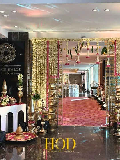A wide view of a grand entrance, combining a floral welcome sign, traditional brass lamps, and hanging flower curtains to create a rich and inviting atmosphere.