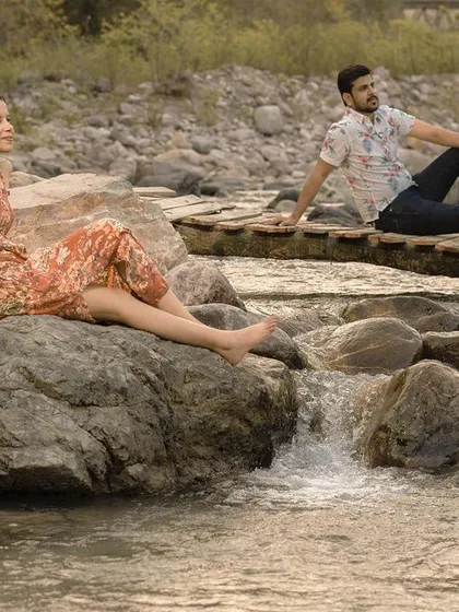 A serene portrait of the couple sitting by a flowing stream, capturing a quiet moment of connection during their outdoor pre-wedding shoot.